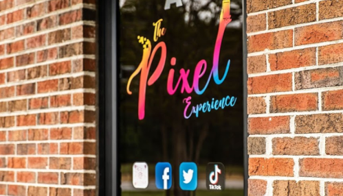 Colorful sign for "The Pixel Experience" on a brick wall, featuring social media icons for Facebook, Twitter, and TikTok.
