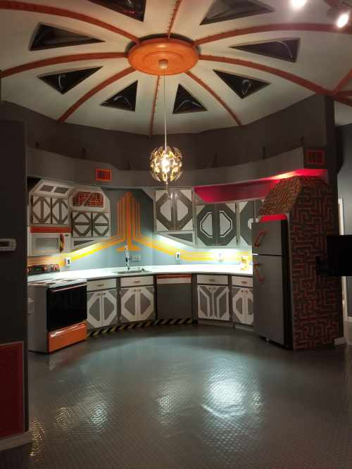Futuristic kitchen with a circular ceiling, colorful accents, and modern appliances in a sleek design.