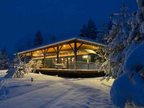 A cozy cabin illuminated at night, surrounded by snow-covered trees and a serene winter landscape.