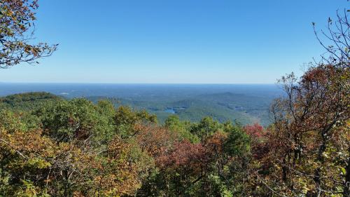 A panoramic view of rolling hills and valleys, with trees displaying autumn colors under a clear blue sky.