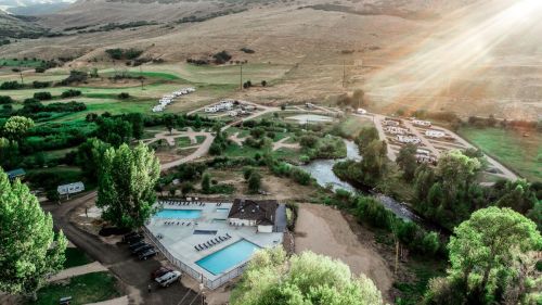 Aerial view of a campground with a pool, surrounded by greenery and hills, with RVs parked nearby and a river flowing.