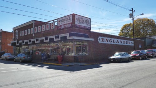 A brick building with "Englanders" signage, featuring a grill and shop, surrounded by parked cars on a sunny day.
