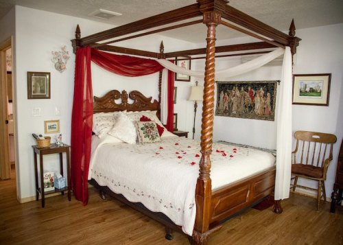 A cozy bedroom featuring a four-poster bed with draped fabric, floral bedding, and rose petals scattered on the sheets.