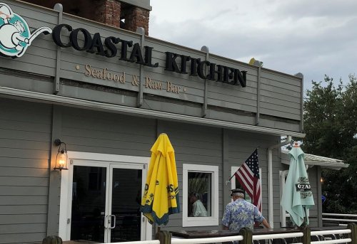 Exterior of Coastal Kitchen, a seafood and raw bar, featuring umbrellas and an American flag.