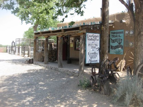 A rustic trading post with a petting zoo sign, surrounded by trees and gravel paths, showcasing local attractions.