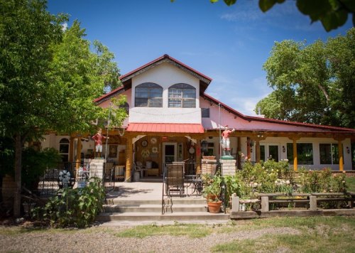 A charming, two-story house with a red roof, surrounded by greenery and a welcoming porch.