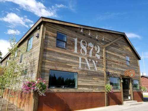 Exterior of the 1872 Inn, a wooden building with large windows and flower baskets, under a blue sky.