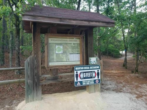 Sign at Sesquicentennial State Park with a map and a social distancing reminder, surrounded by trees.