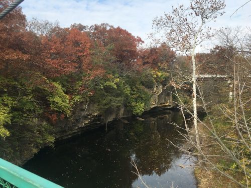 A serene river flows between rocky cliffs, surrounded by trees with autumn foliage in shades of red and yellow.