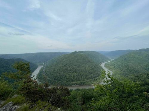 A panoramic view of lush green hills surrounding a winding river under a cloudy sky.