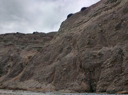 A rugged, sandy cliff with layered rock formations under a cloudy sky.