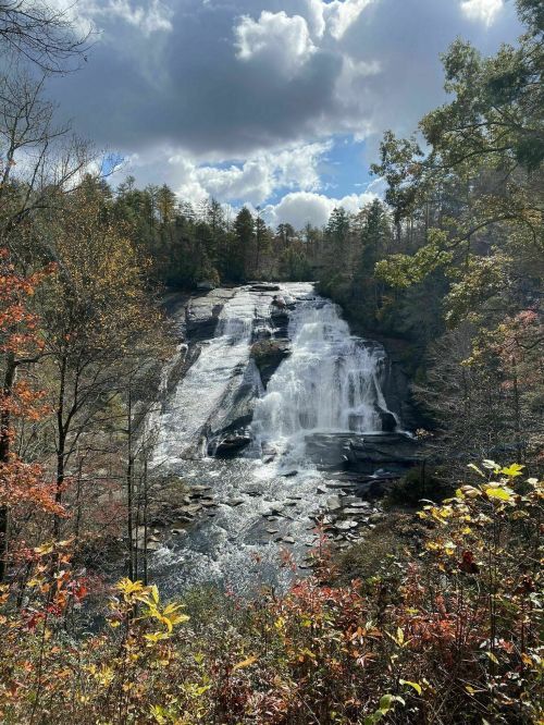 A scenic waterfall cascades down rocky cliffs, surrounded by autumn foliage and a cloudy sky.