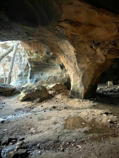 A rocky cave interior with large stone formations and natural light streaming in from the entrance.