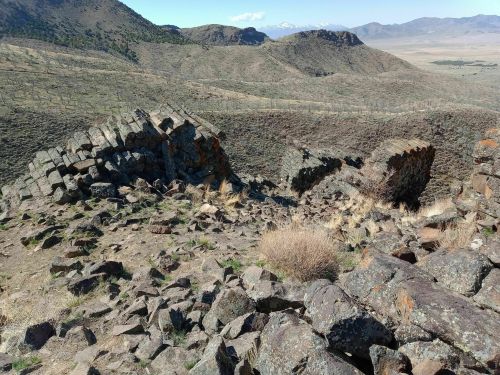 A rocky landscape with scattered boulders and distant mountains under a clear blue sky.
