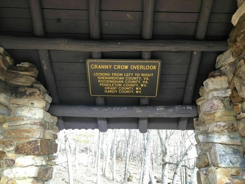Sign at Cranny Crow Overlook, listing nearby counties in Virginia and West Virginia, under a stone shelter.