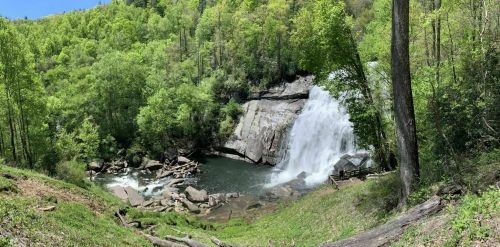 A scenic waterfall surrounded by lush green trees and rocky terrain under a clear blue sky.