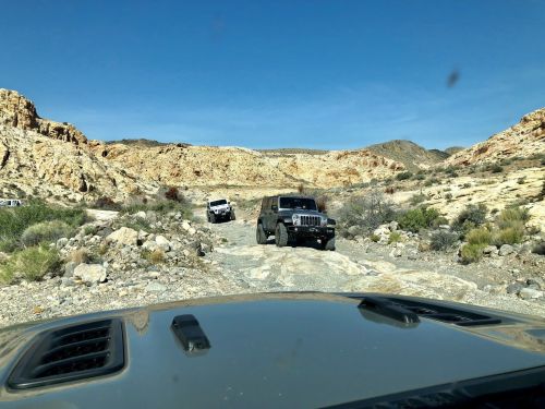 Two off-road vehicles navigate a rocky trail in a desert landscape under a clear blue sky.