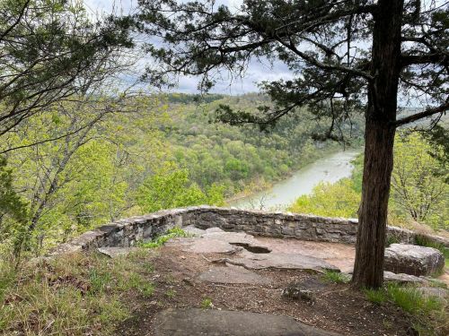 A scenic view from a rocky overlook, featuring a winding river and lush green trees in the background.