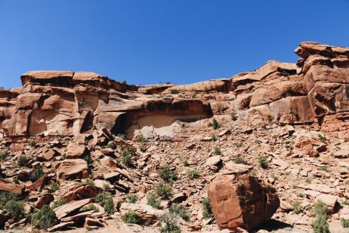 Rocky cliffside with layered sandstone formations and sparse vegetation under a clear blue sky.