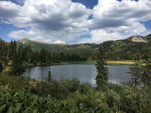 A serene lake surrounded by lush greenery and mountains under a partly cloudy sky.