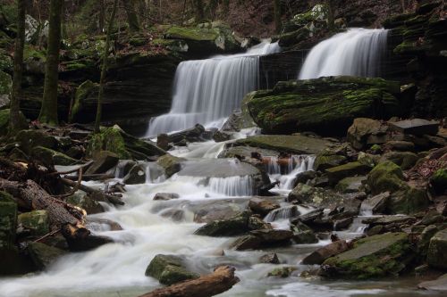 A serene waterfall cascades over moss-covered rocks, surrounded by lush greenery and flowing water.