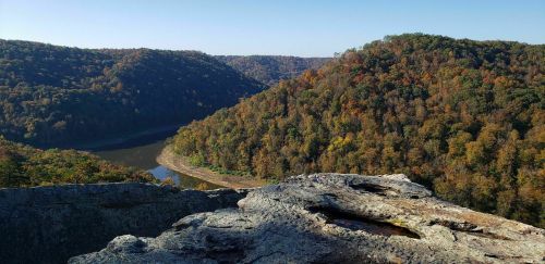 A scenic view of rolling hills with autumn foliage and a winding river below, captured from a rocky overlook.