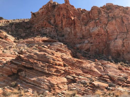 Rocky red cliffs with layered formations and sparse vegetation under a clear blue sky.