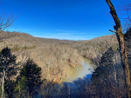 A scenic view of a winding river surrounded by bare trees and rolling hills under a clear blue sky.