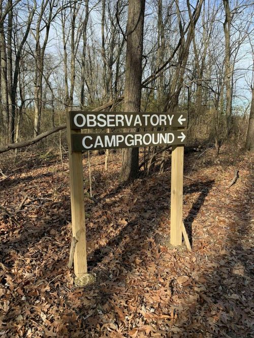 Wooden signpost in a wooded area pointing left to "Observatory" and right to "Campground," surrounded by fallen leaves.