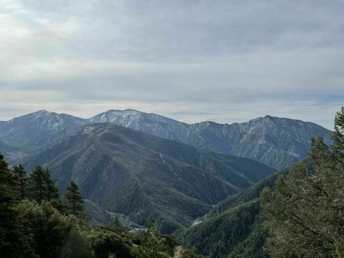 A panoramic view of green mountains under a cloudy sky, showcasing rugged peaks and a serene landscape.