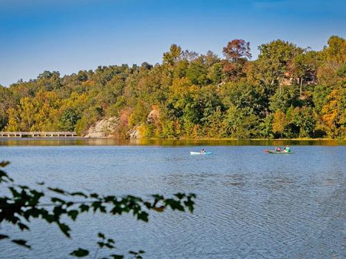 Two kayakers paddle on a calm lake surrounded by colorful autumn trees and a clear blue sky.
