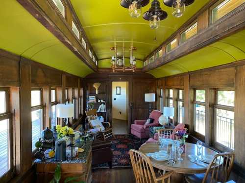 Interior of a vintage train car, featuring wooden walls, green ceiling, dining area, and cozy seating with natural light.