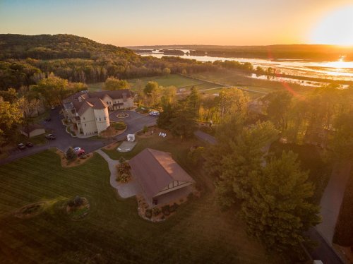 Aerial view of a scenic landscape at sunset, featuring a large building, lush greenery, and a river in the background.