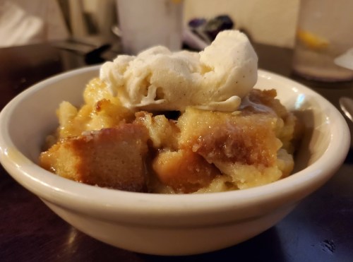 A bowl of bread pudding topped with a scoop of vanilla ice cream.