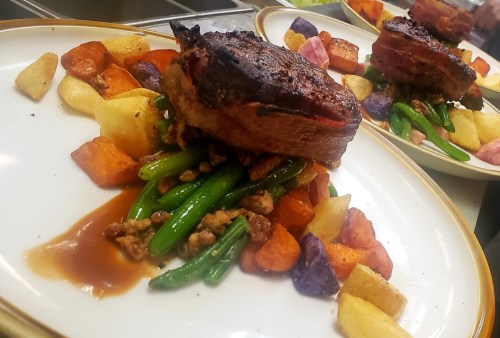 A beautifully plated dish featuring roasted meat atop green beans and colorful roasted vegetables.