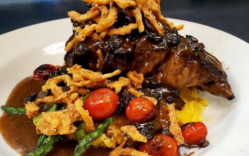 A plate of tender meat topped with crispy onions, cherry tomatoes, and asparagus, served over creamy polenta.