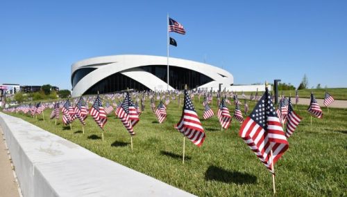 A modern building with a curved design surrounded by a field of small American flags on a sunny day.