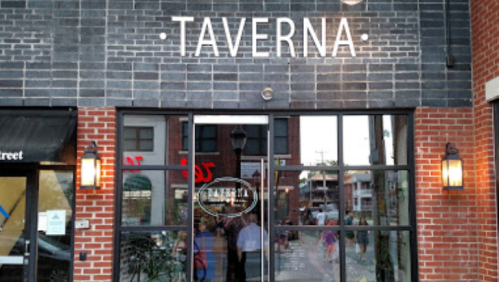 Exterior view of a restaurant named "Taverna," featuring a glass entrance and brick facade.