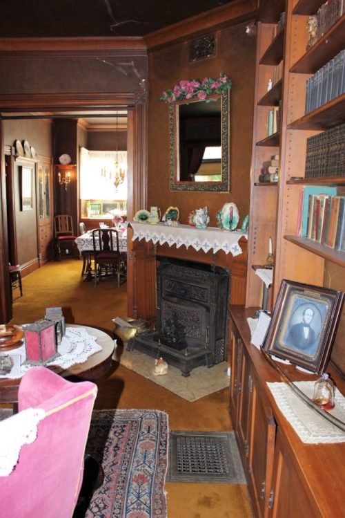 Cozy vintage living room with a fireplace, bookshelves, and a mirror, featuring warm colors and classic decor.