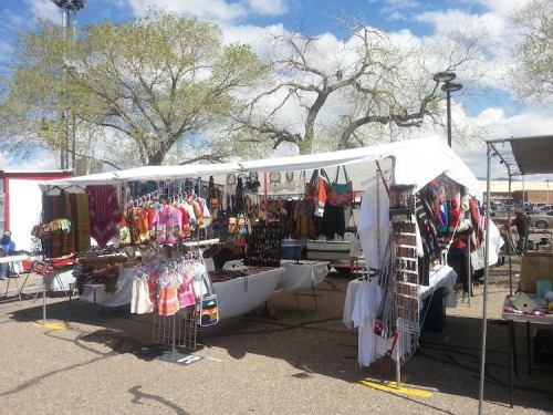 A vibrant market stall with colorful clothing and accessories displayed under a white tent on a sunny day.