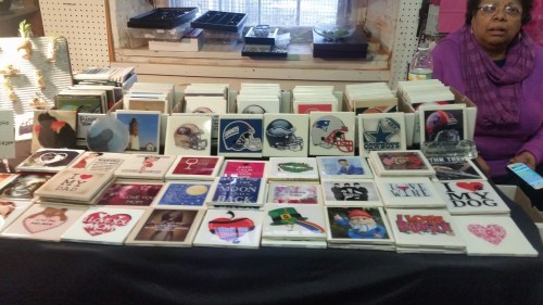A display of various greeting cards and coasters on a table, with a woman sitting nearby, looking at her phone.
