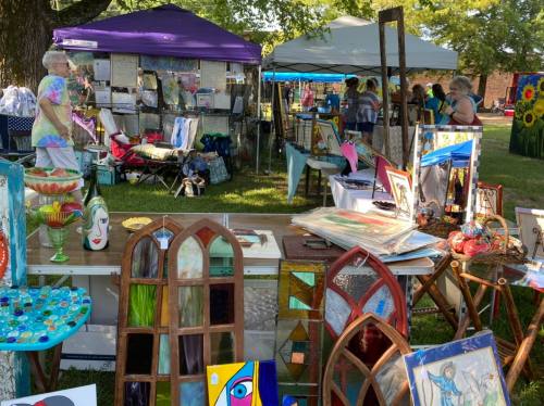 A vibrant outdoor art fair with colorful displays, tents, and people browsing various artworks and crafts.