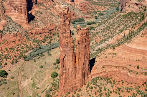 Aerial view of towering red rock formations amidst a desert landscape with green vegetation and winding paths.