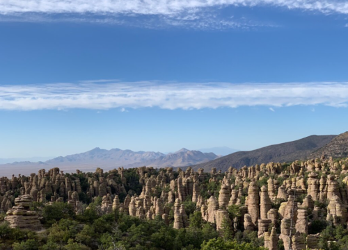 A panoramic view of unique rock formations surrounded by greenery under a clear blue sky with distant mountains.