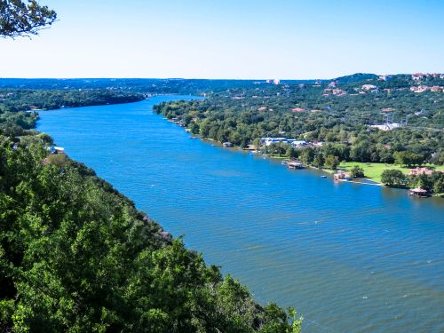 A scenic view of a wide river surrounded by lush greenery and hills under a clear blue sky.
