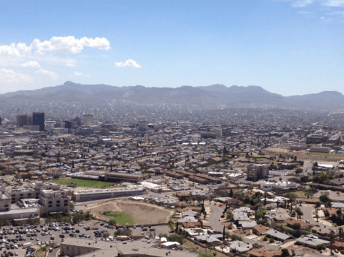Aerial view of a sprawling city with mountains in the background under a clear blue sky.