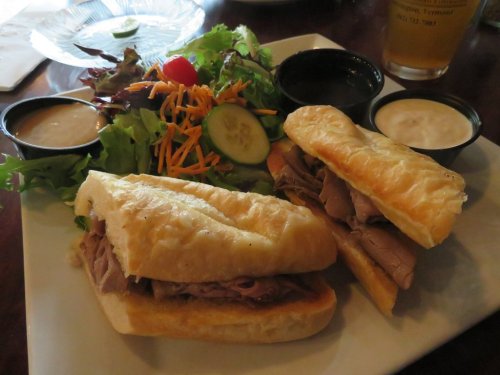 A plate with two roast beef sandwiches and a side salad, accompanied by two dipping sauces.