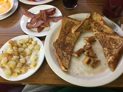 A plate with French toast, bacon, and diced potatoes on a wooden table.