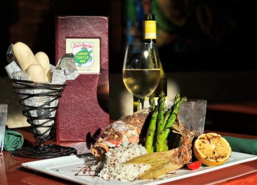 A plate of grilled fish with asparagus, rice, and a lemon slice, accompanied by a glass of white wine and breadsticks.