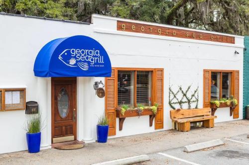 Exterior of Georgia Sea Grill, featuring a blue awning, wooden door, and planters, with a bench outside.